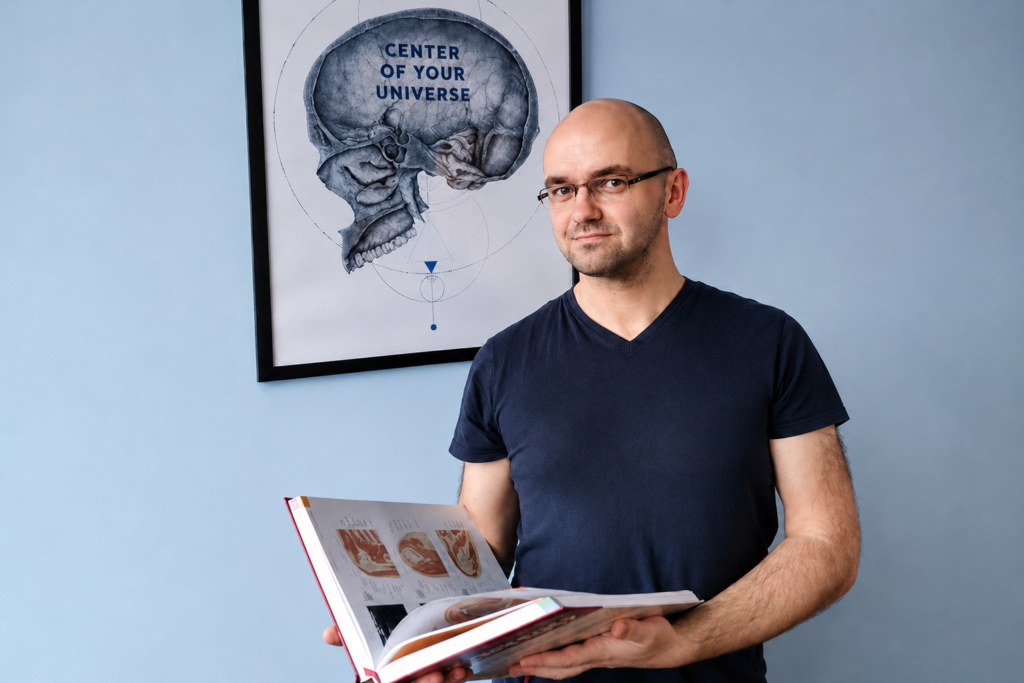 Krzysztof Szpakowski z atlasem anatomicznym w gabinecie masażu REHKOS w Szczecinie